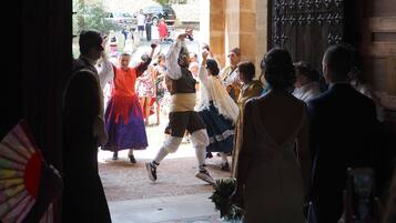 Un groupe de personnes, vêtues de costumes traditionnels, danse dans une cour dallée, bordée d’un mur de pierre.