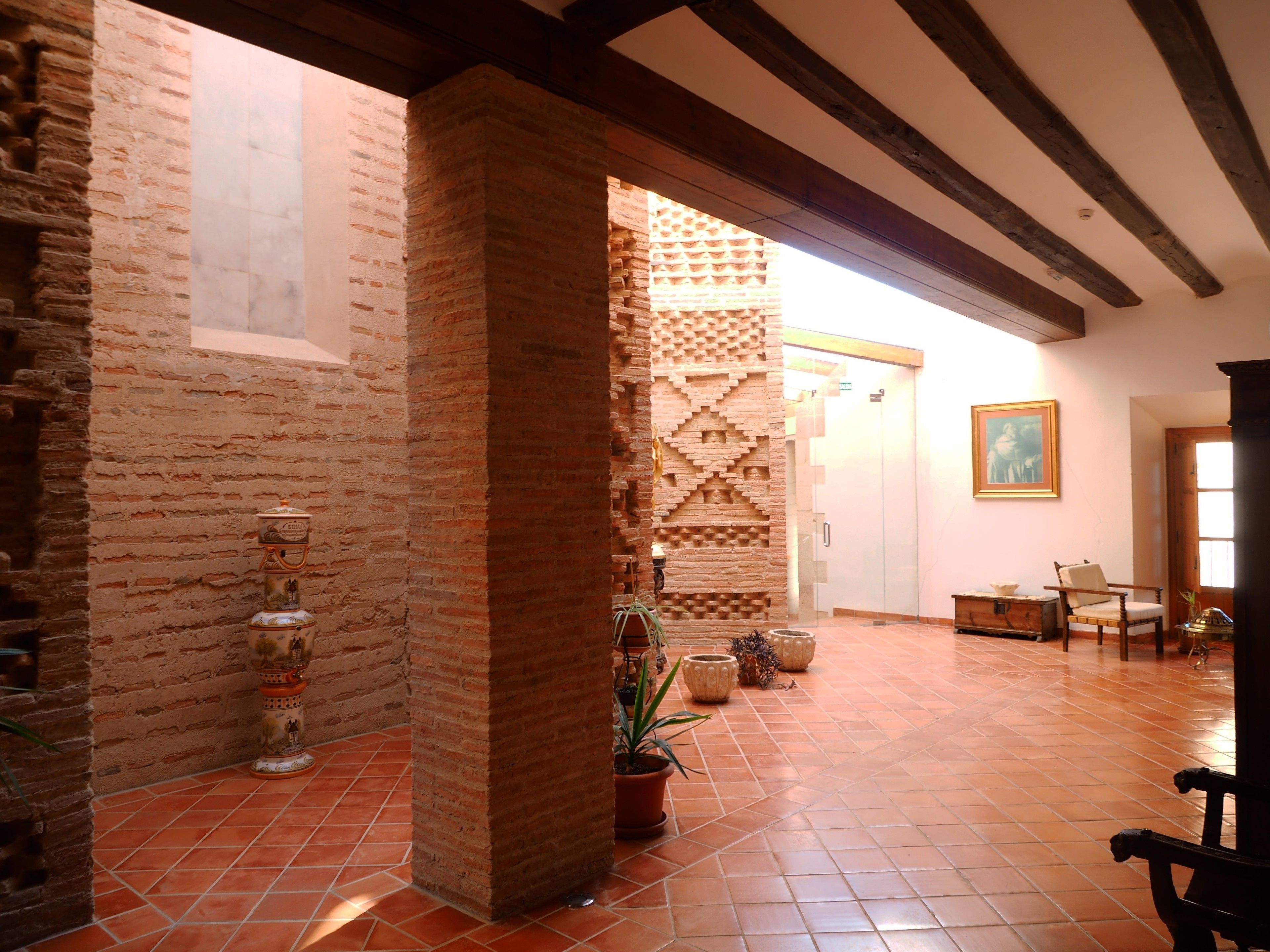 Una habitación amplia con vigas de madera a la vista, suelo de baldosas y paredes de ladrillo y enlucido.