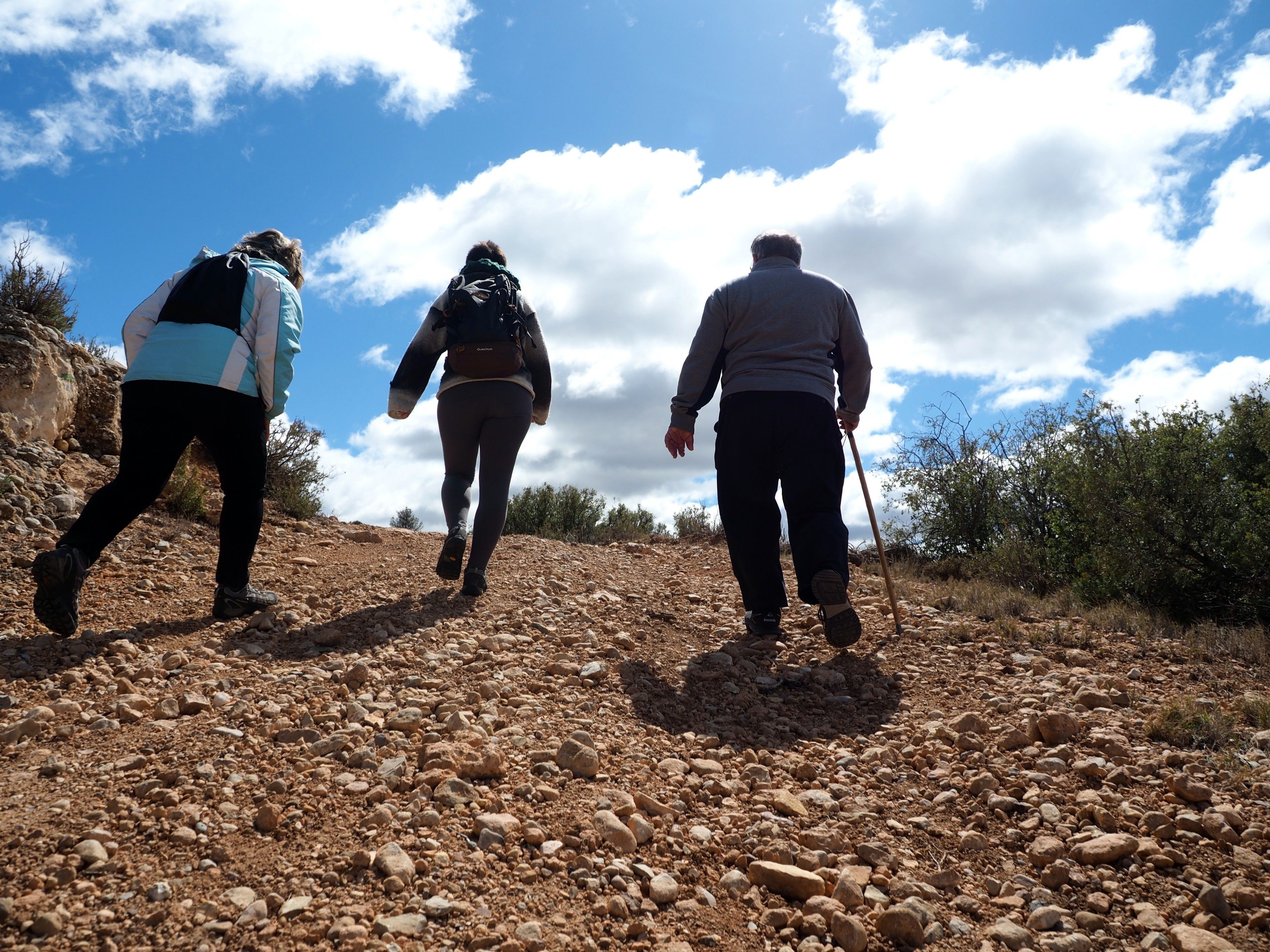 Three people hiking on a rocky trail with a clear sky.