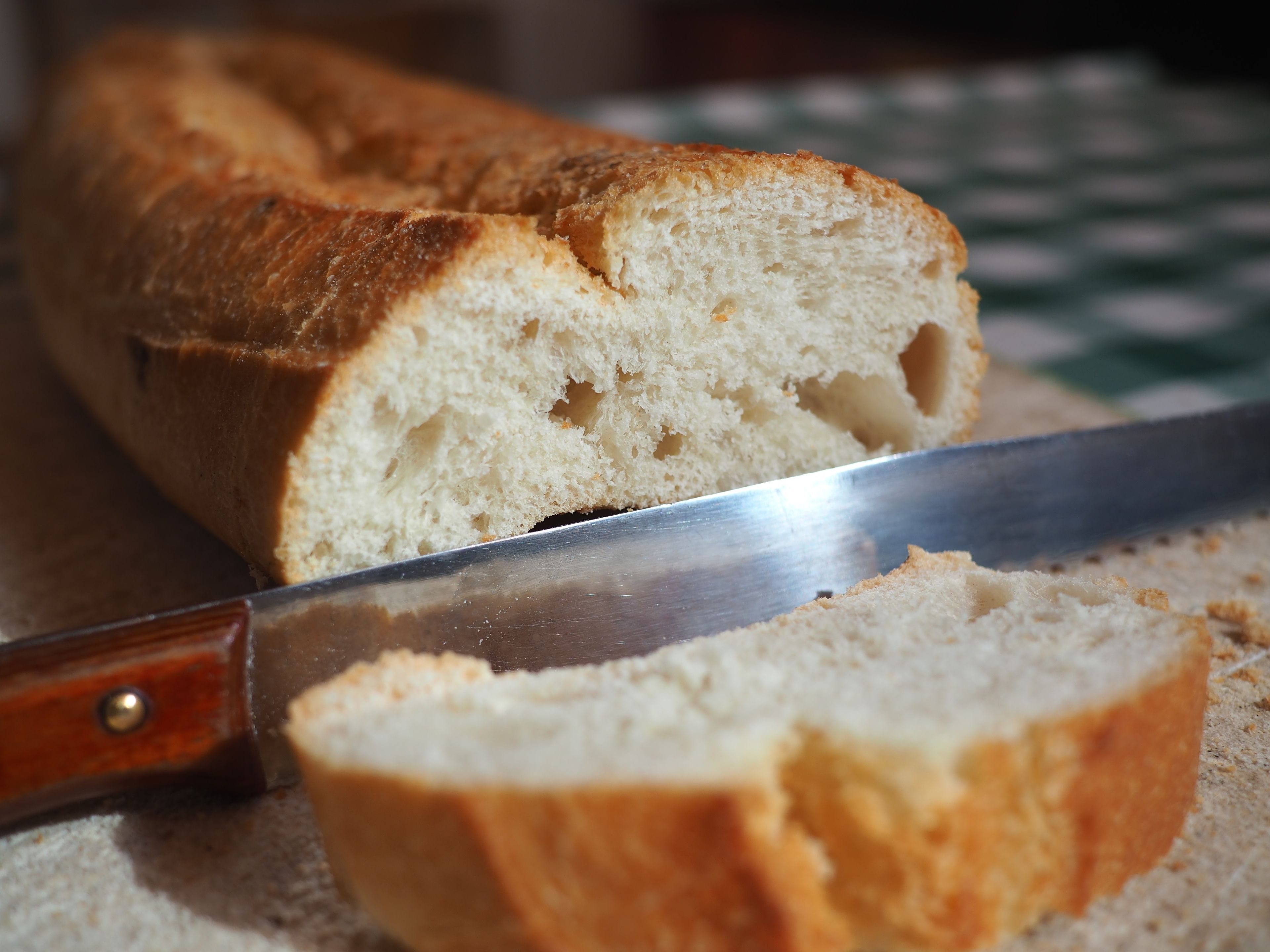 Una hogaza de pan con un cuchillo cortándola, sobre un mantel a cuadros.
