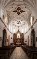 Interior de iglesia con techo abovedado alto, decoraciones ornamentales y un altar central.