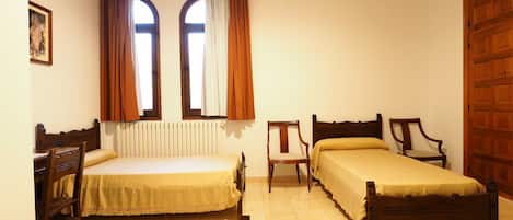 A bedroom with two wooden beds, a chair, a wooden wardrobe, and a window with curtains.