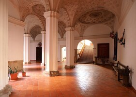 Un interior espacioso con techos altos, columnas ornamentales y una escalera central que conduce a un nivel superior.