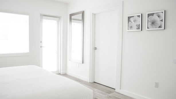 A minimalist bedroom with a large bed, a door, and two framed pictures on the wall. - Sobe Lux (Miami Beach)