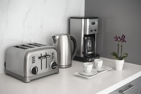 A kitchen counter with a silver toaster, a stainless steel coffee maker, and a potted orchid.