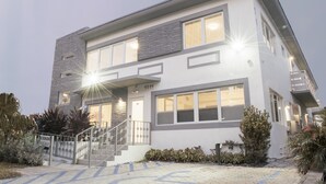 A modern two-story building with a staircase leading to the entrance, a well-lit front porch, and a paved driveway. - Sobe Lux (Miami Beach)