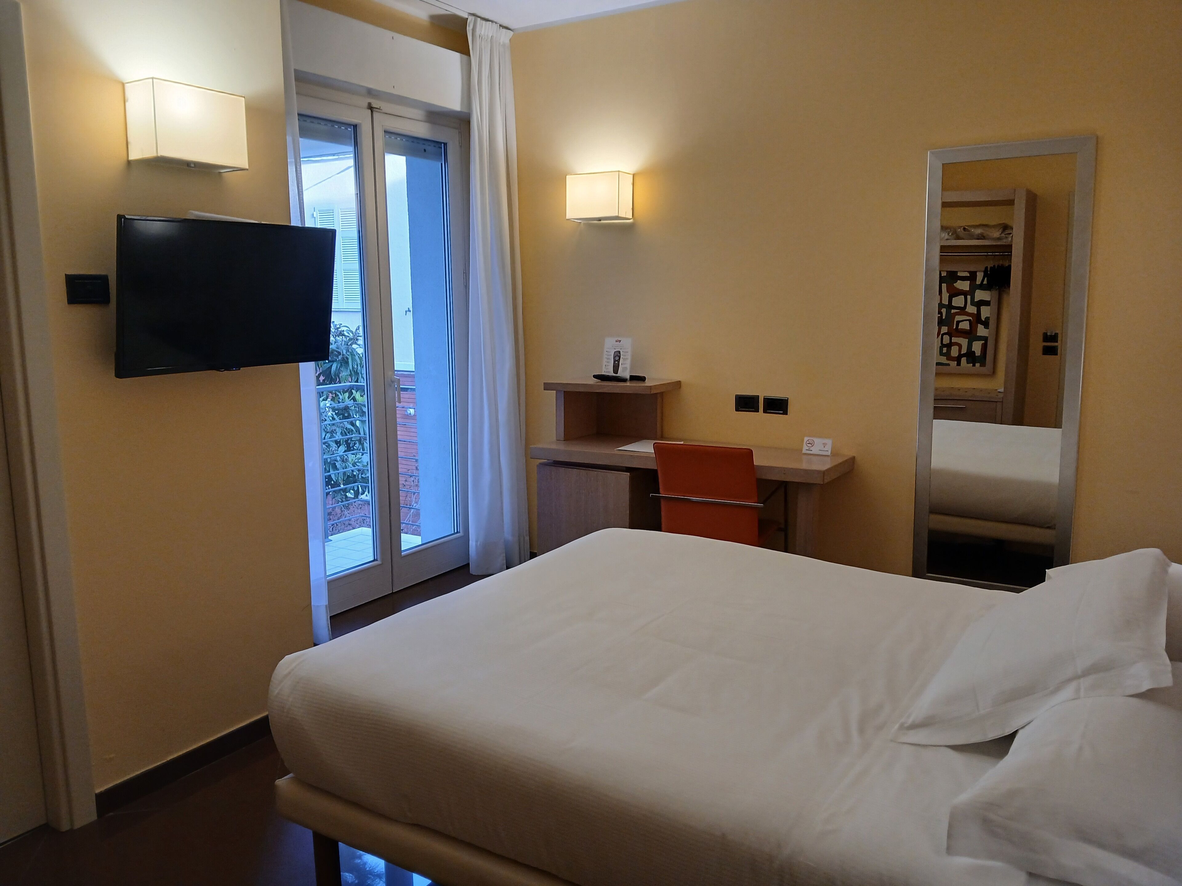 Une chambre d’hôtel comprenant un lit, un bureau, une chaise, une télévision, une fenêtre avec des rideaux et un miroir.