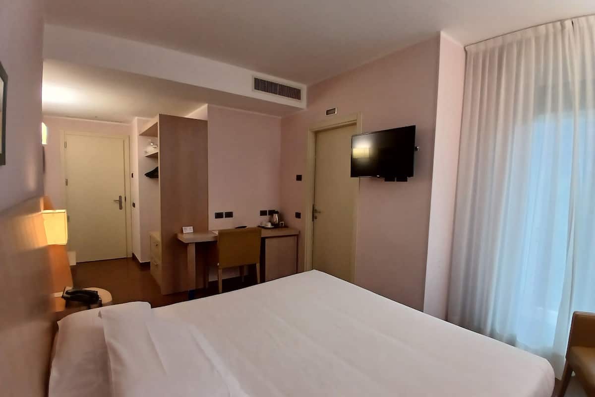 Een hotelkamer met een bed, een bureau, een stoel, een televisie en een deur.
