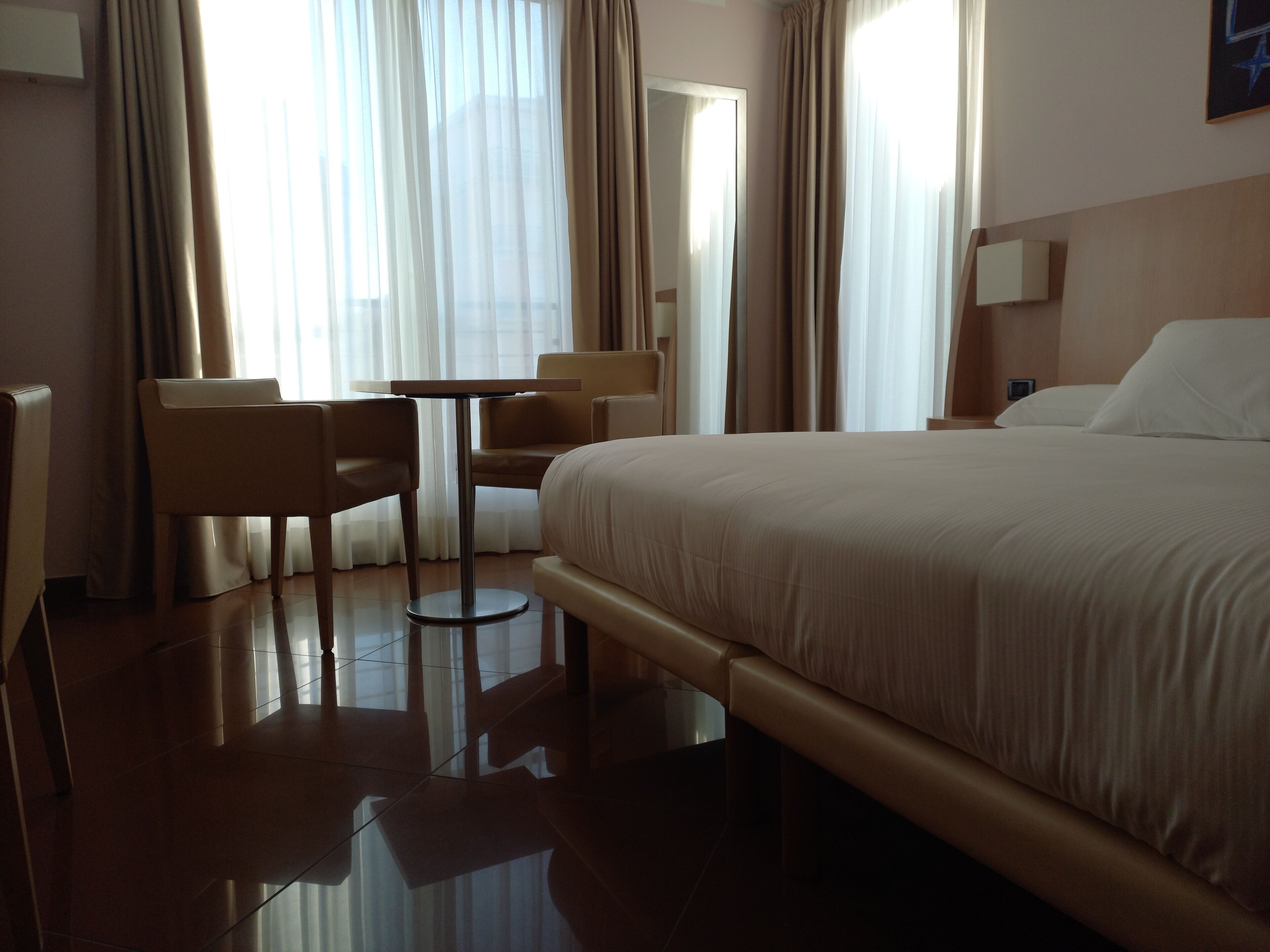 Habitación de hotel con cama, una silla, una mesita y un espejo.