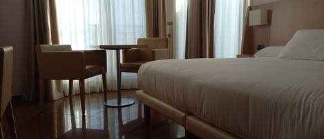 Habitación de hotel con cama, una silla, una mesita y un espejo.