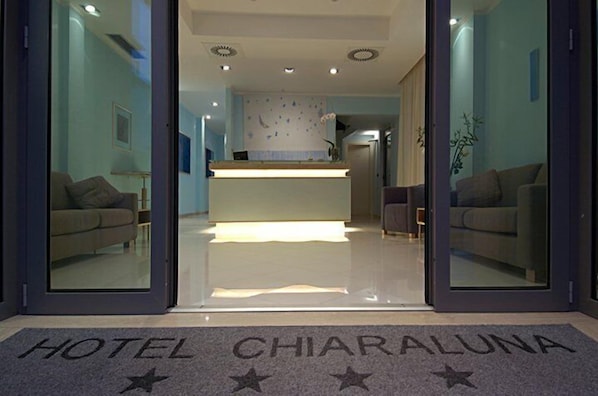A hotel entrance with a reception desk, sofas, and a clear view of the interior.