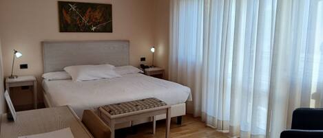 A hotel room with a bed, bedside tables, a desk, a chair, and a painting on the wall.