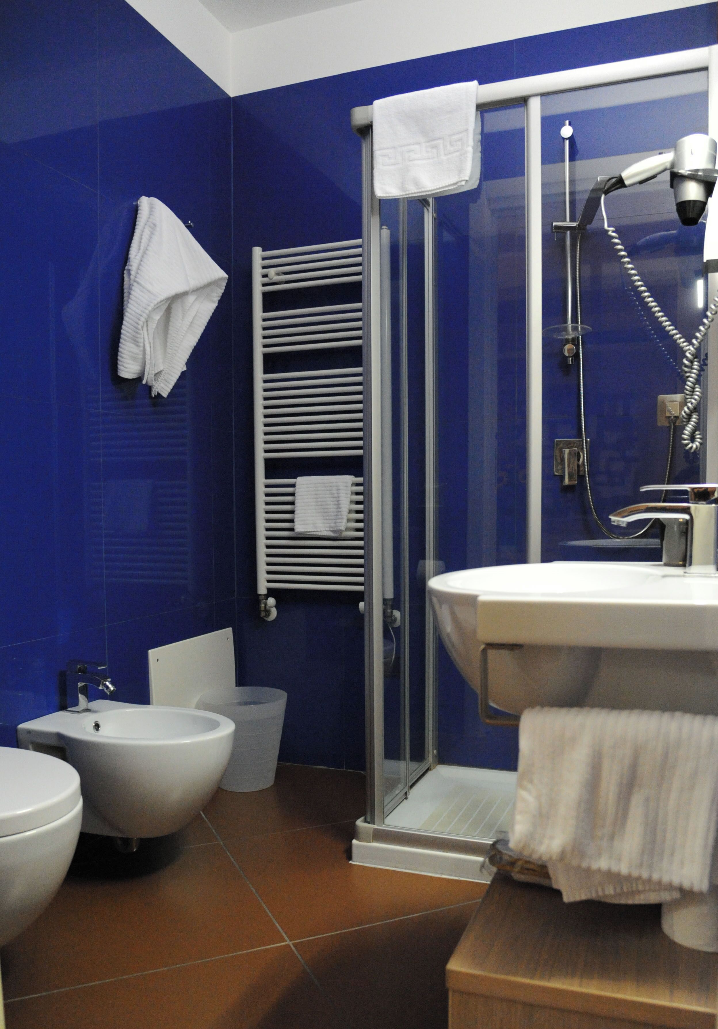 A bathroom with a glass shower enclosure, a white sink, and two bidets.