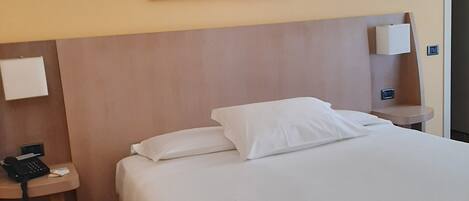 Habitación de hotel con una cama grande, cabecero, mesita de noche con teléfono, lámpara de pared y un cuadro sobre la cama.