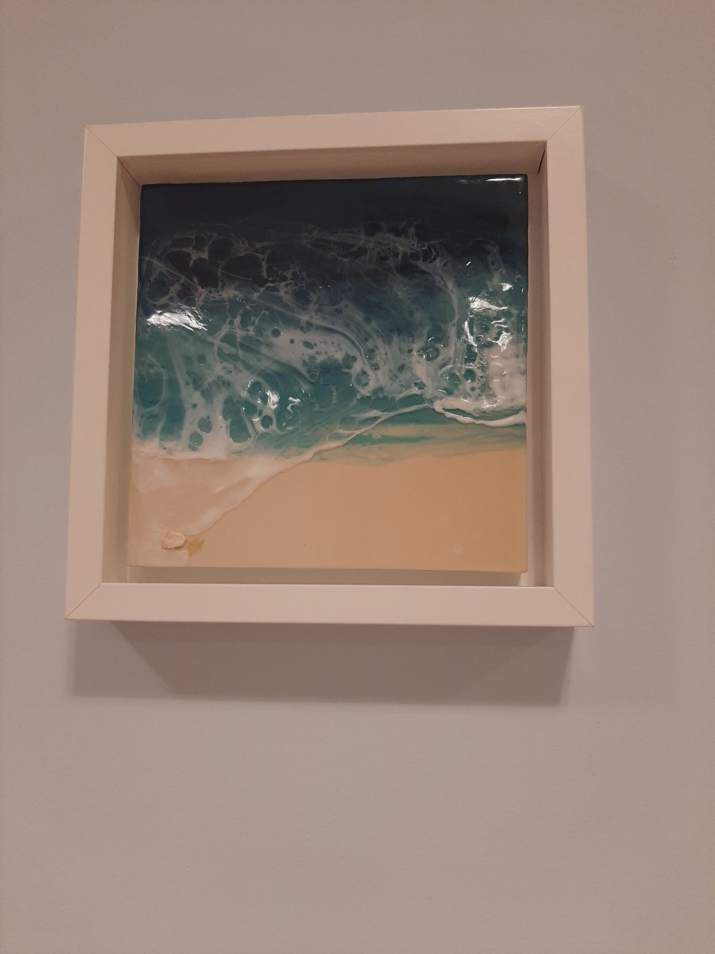 Una obra enmarcada que muestra una ola rompiendo sobre una playa arenosa.