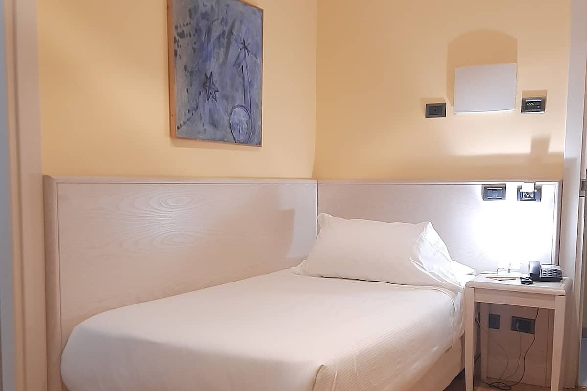 Een slaapkamer met een groot bed, een nachtkastje met een telefoon en een wandlamp.