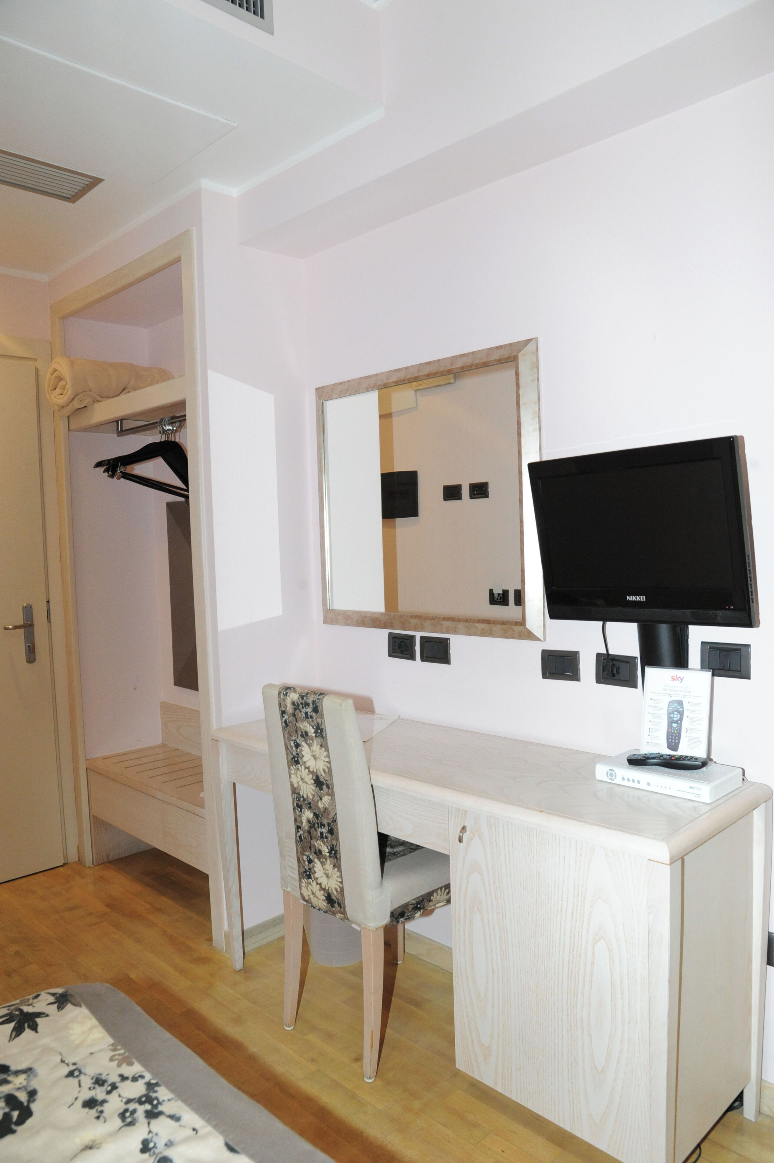 Una habitación con cama, escritorio, silla, televisor y espejo.