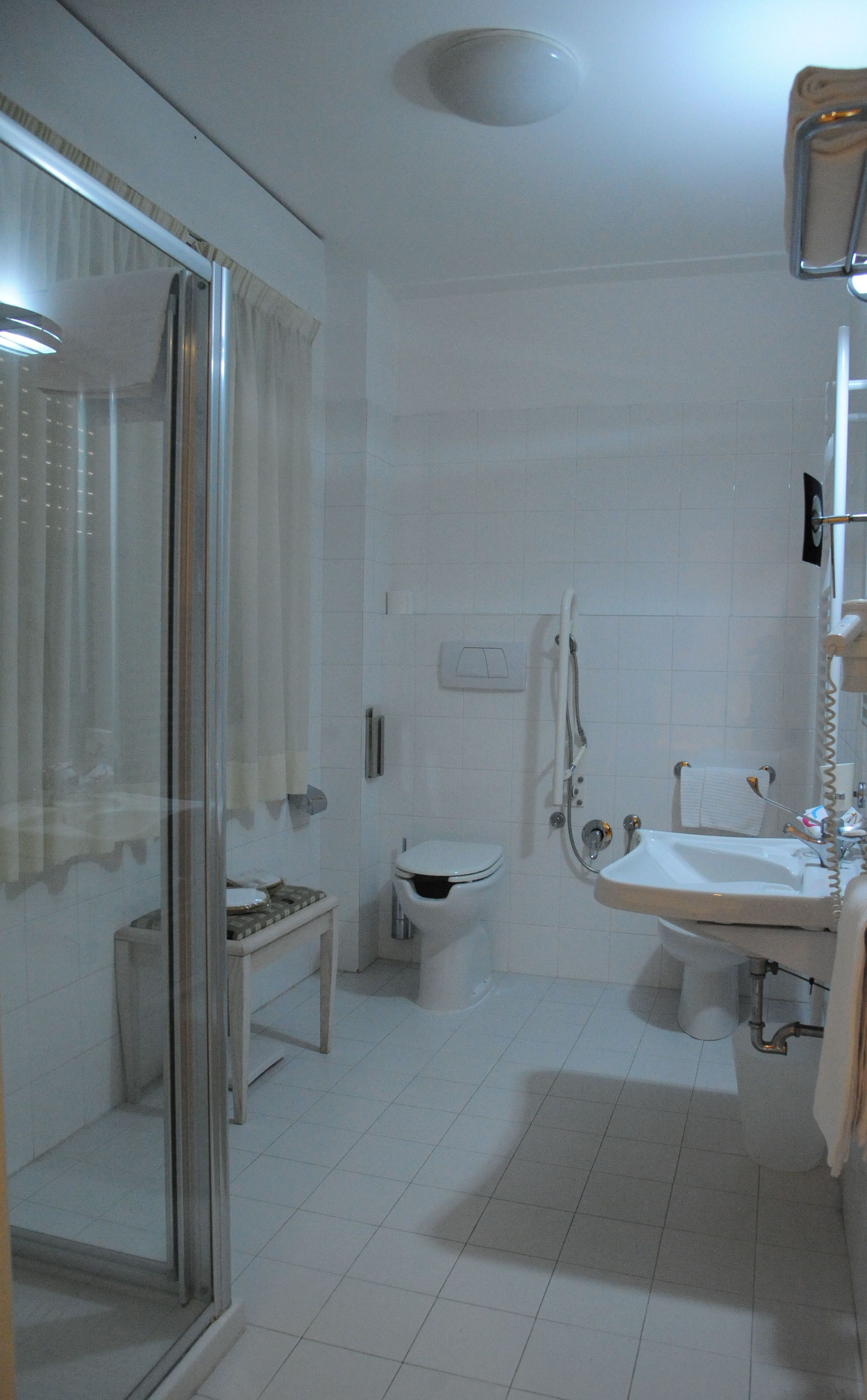 Un baño con cabina de ducha de vidrio, un inodoro y un lavabo con toallero.