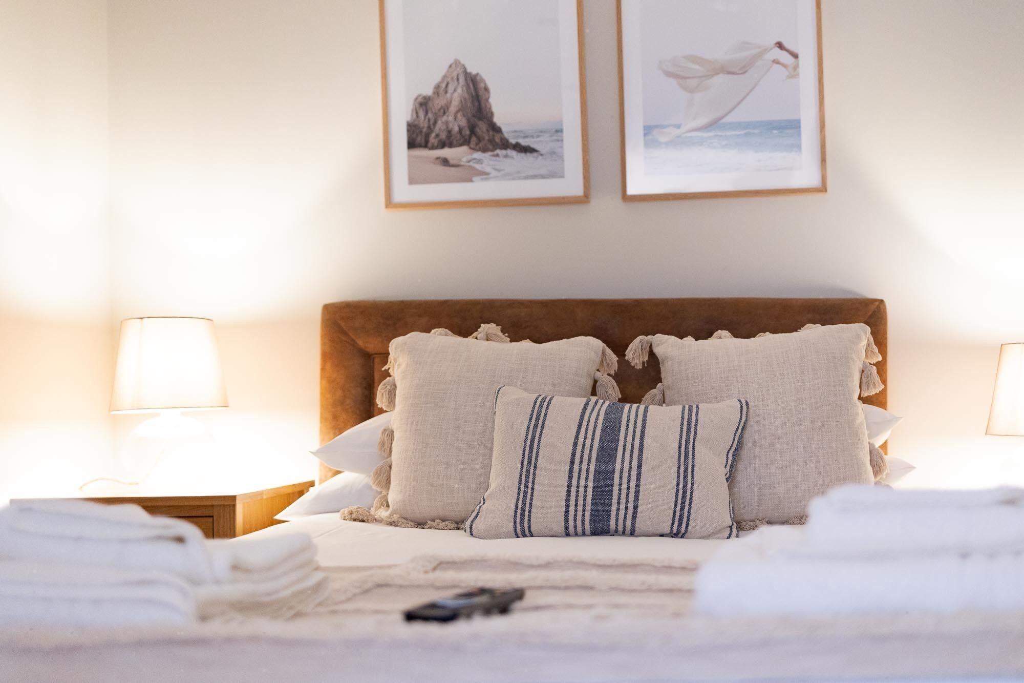 A neatly made bed with pillows and a blanket, two framed pictures on the wall, and bedside lamps.