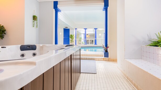A modern bathroom with a large bathtub, a small sink, and a view of an indoor pool area. - Red Lea Apartments (Scarborough)