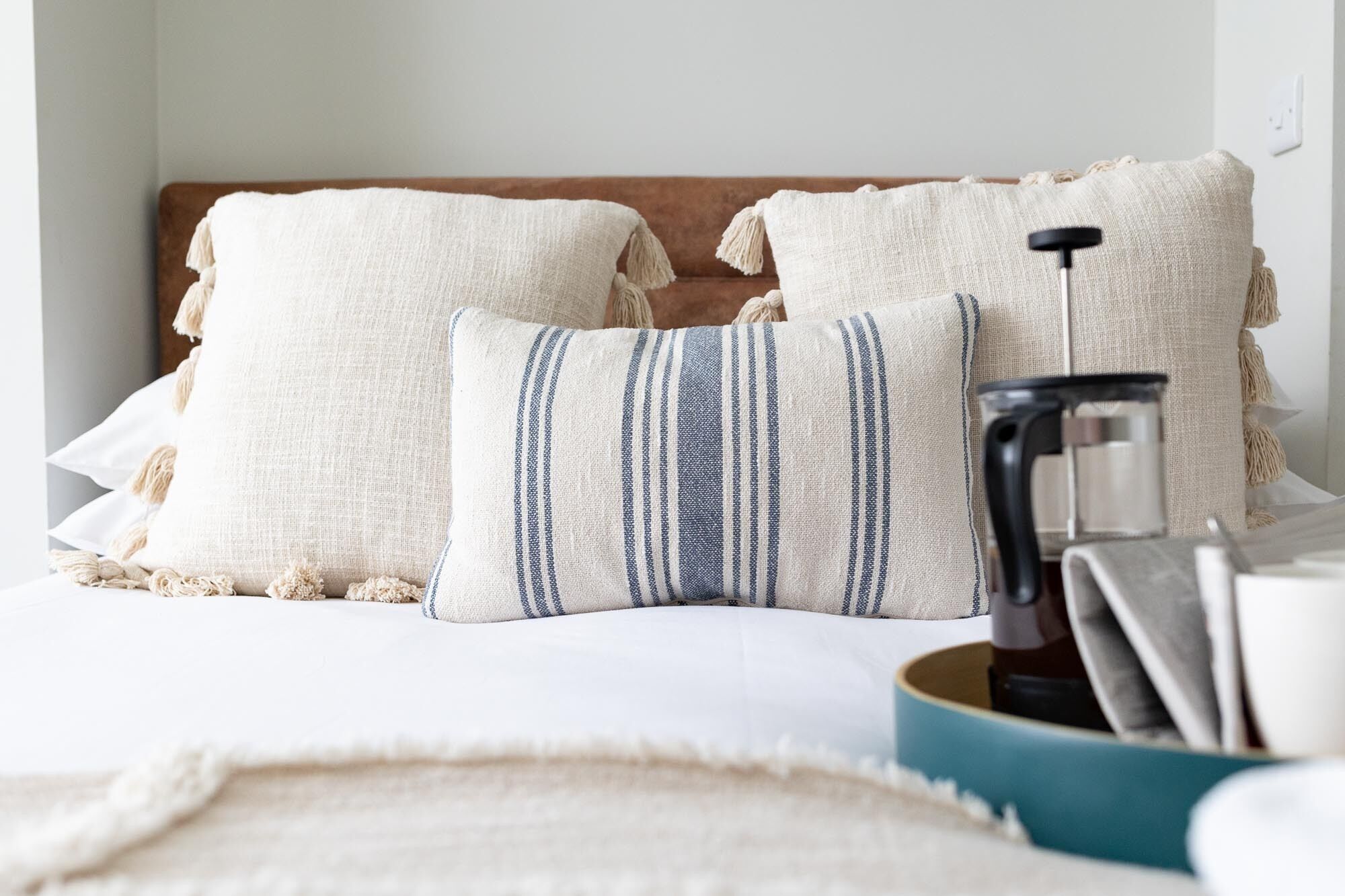 Ein Bett mit zwei Kissen, einfarbig und gestreift, sowie ein Tisch mit einer Kaffeemaschine.