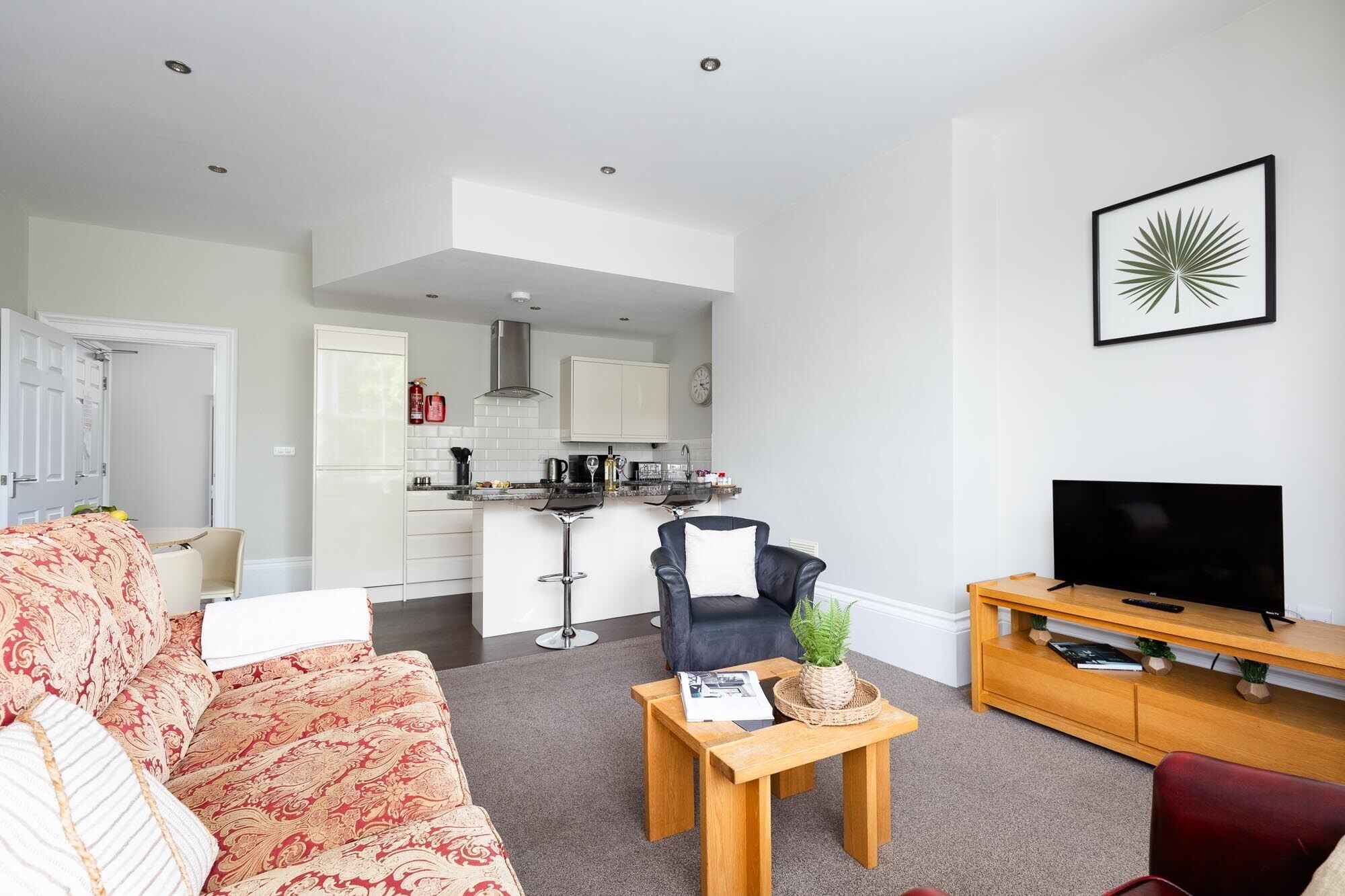 A modern living room with a sofa, a coffee table, a TV, and a kitchen in the background.