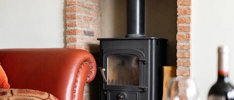 A cozy living room with a brick fireplace, a leather sofa, and a table with a wine glass and a book.
