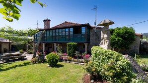 A two-story stone house with a balcony, surrounded by a well-maintained garden with various plants and flowers. - Casa de Marcelo (Padron)