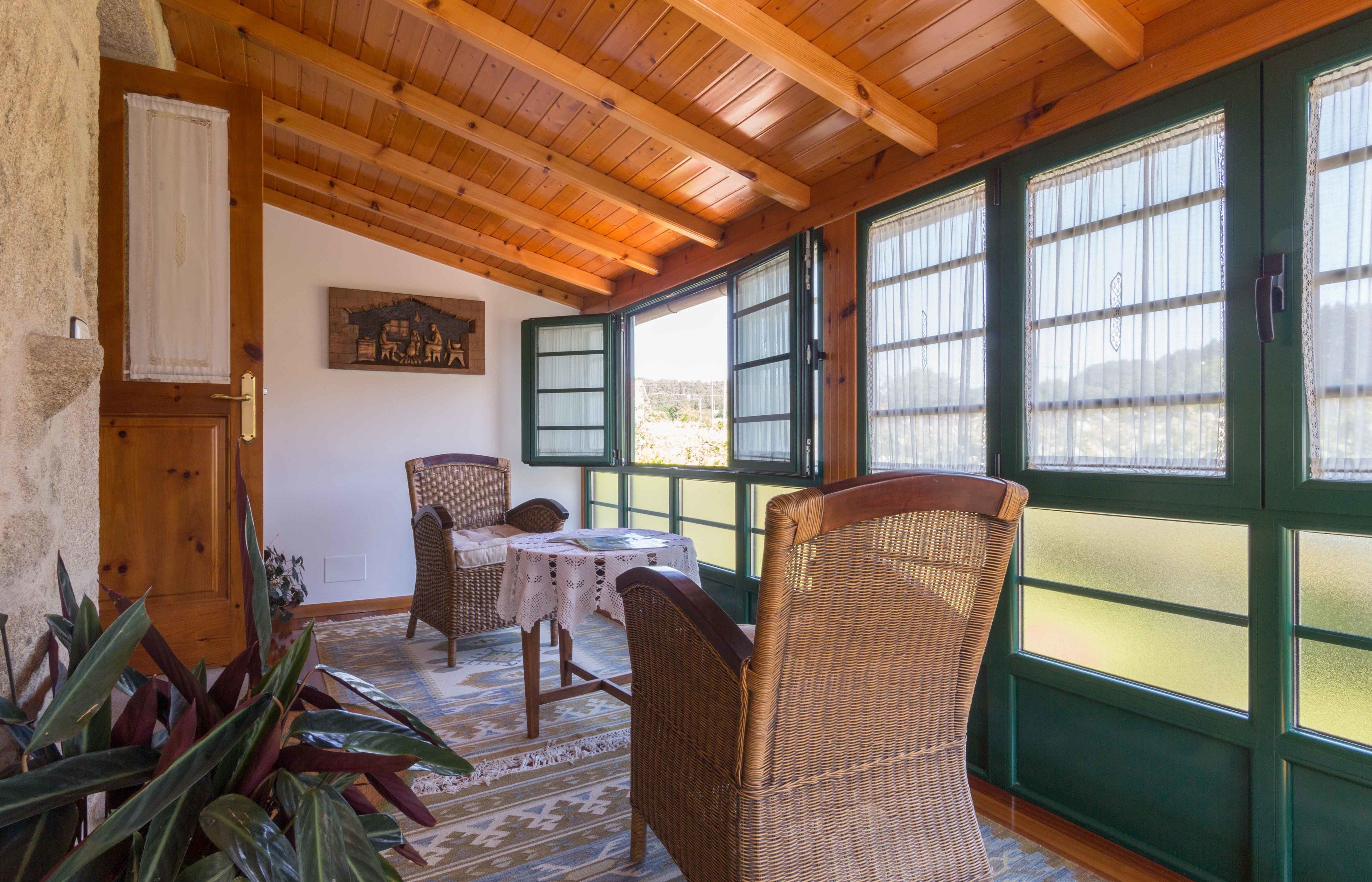 Una habitación acogedora con vigas de madera, mobiliario de mimbre y amplios ventanales con contraventanas verdes.