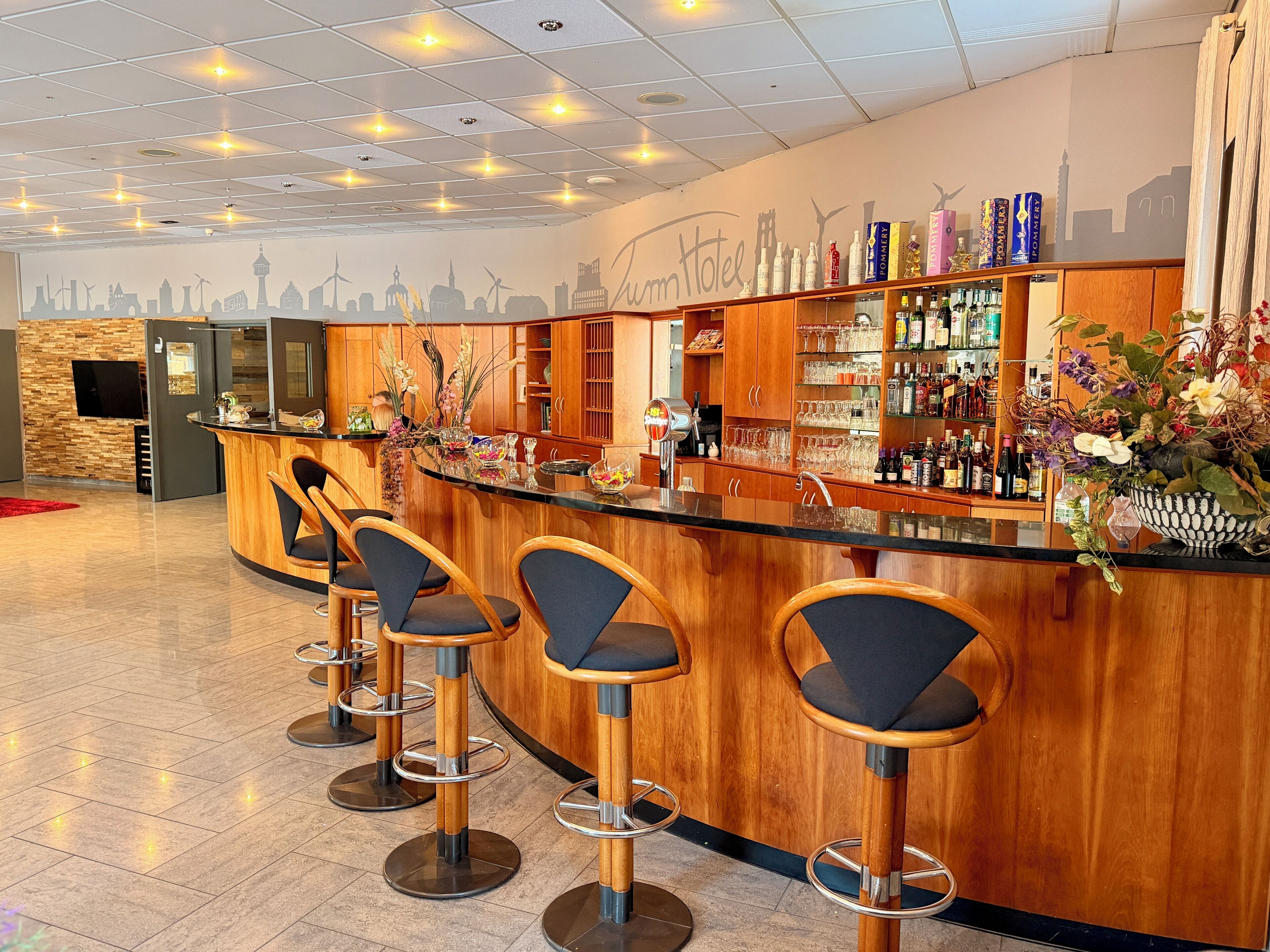 A bar area with wooden stools, a counter with a minibar, and a wall with a cityscape mural.