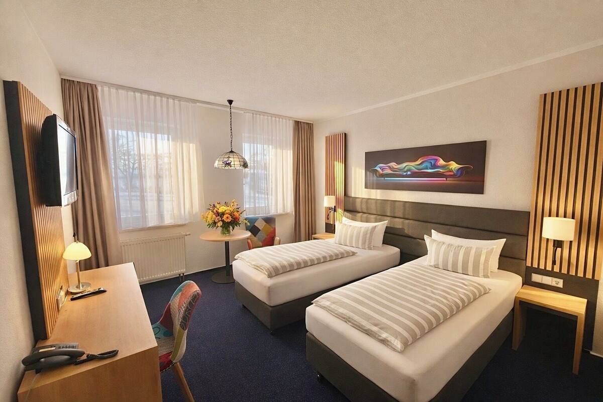 Une chambre d’hôtel avec deux lits, un bureau, une chaise, une télévision et un tableau au mur.