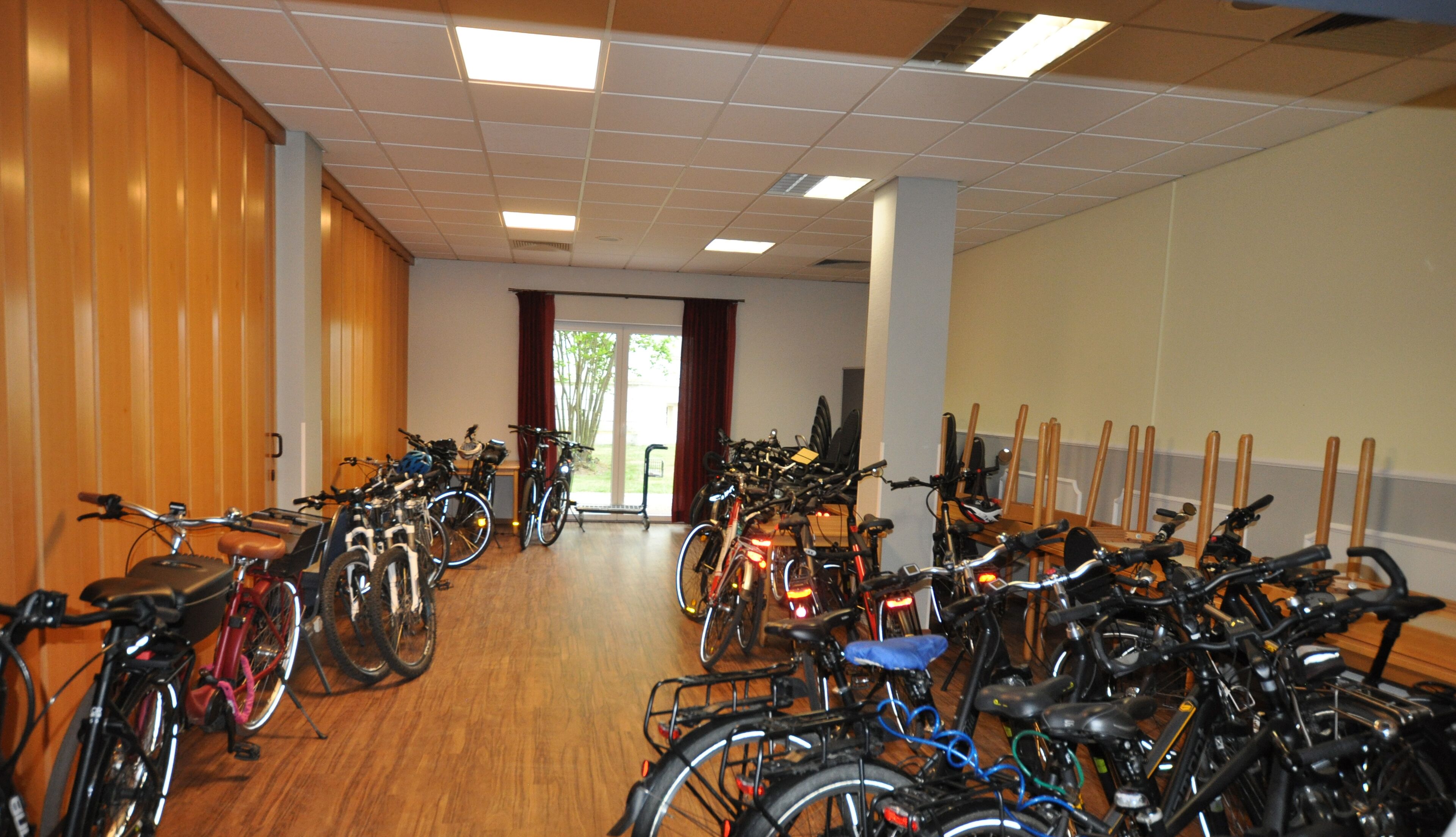 A room with multiple bicycles parked against the walls, a wooden floor, and a door leading outside.