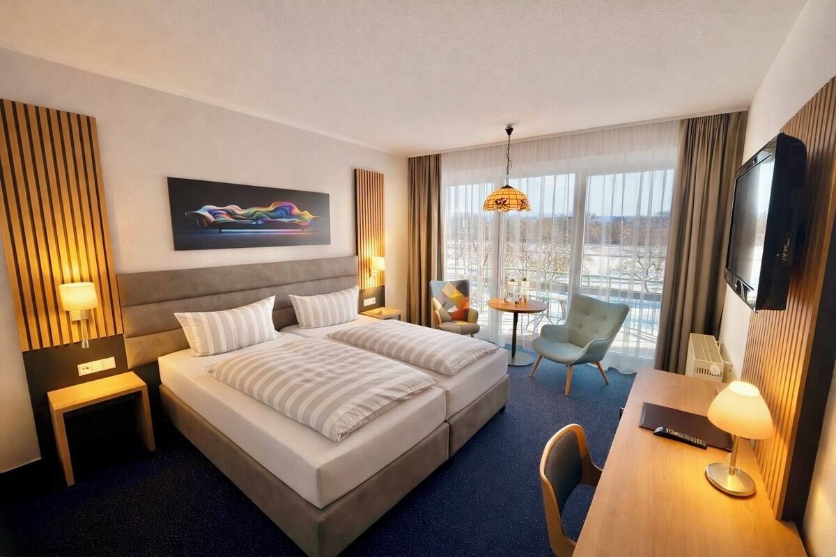 Une chambre d’hôtel avec un grand lit, deux tables de chevet, un bureau avec une chaise, une télévision et une grande fenêtre donnant sur un beau paysage.