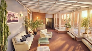 A sunlit room with a sofa, chairs, and a coffee table, featuring large windows and potted plants. - Turmhotel Schwedt (Schwedt/Oder)