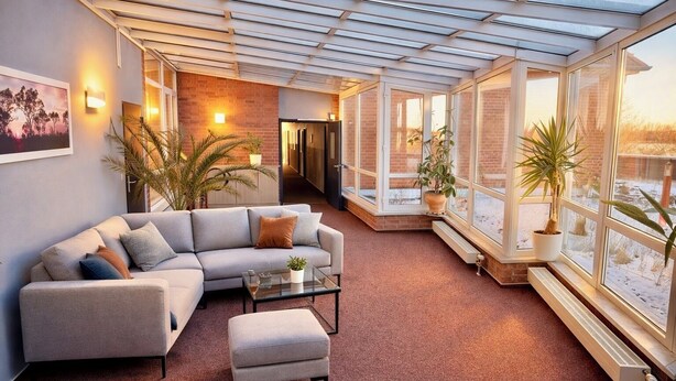 A modern living room with a glass ceiling, a grey sofa, a coffee table, and potted plants. - Turmhotel Schwedt (Schwedt/Oder)