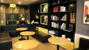 Uma área de estar moderna com assentos em couro preto, mesas de madeira e uma estante repleta de livros e objetos decorativos.