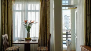 Uma sala de jantar com mesa, cadeiras, um vaso com flores e uma janela com cortinas.