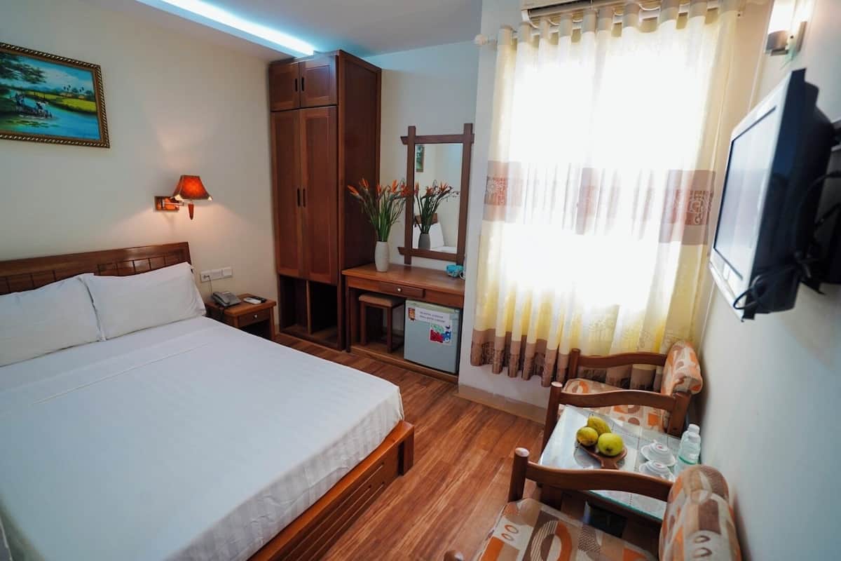 Een hotelkamer met een bed, bureau, stoel en een klein tafeltje met fruit en een fles.