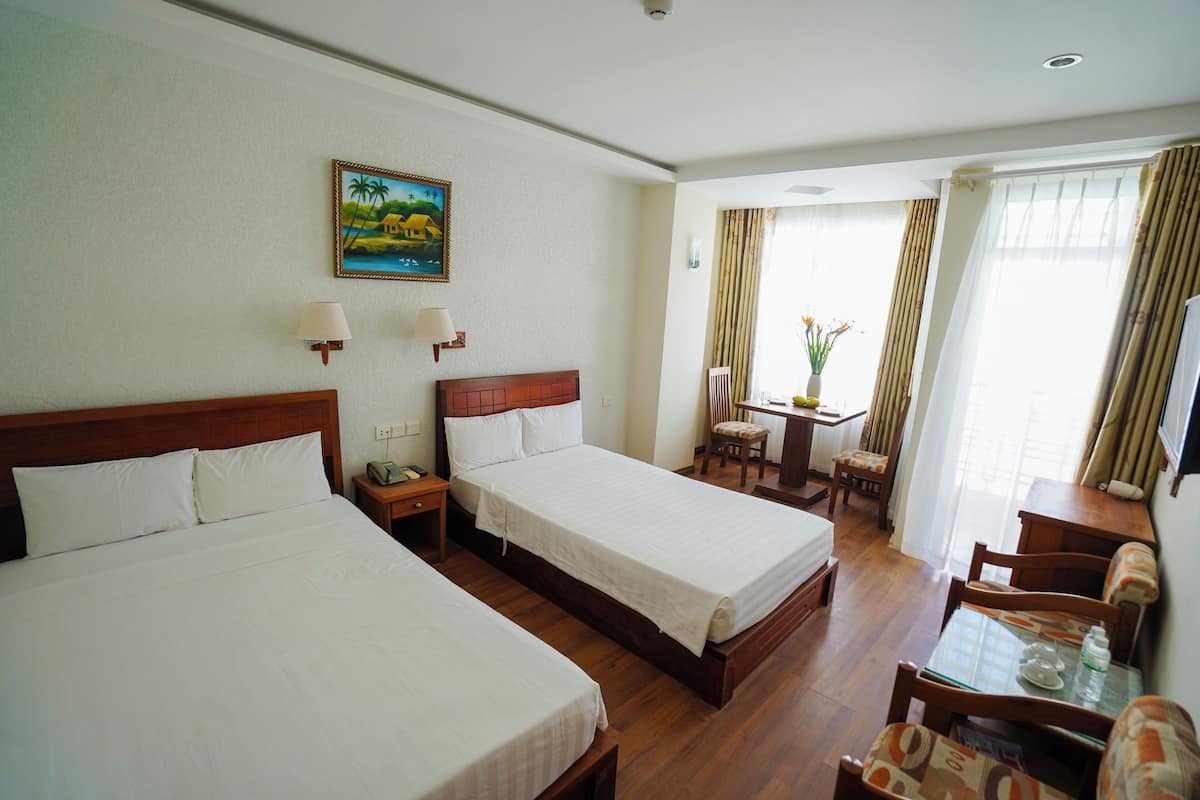 Een hotelkamer met twee bedden, een bureau met stoel, een kleine tafel met vaas en een schilderij aan de muur.