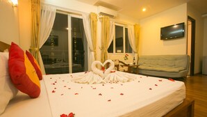 Quarto de hotel com cama, sofá, televisão e janela com cortinas.