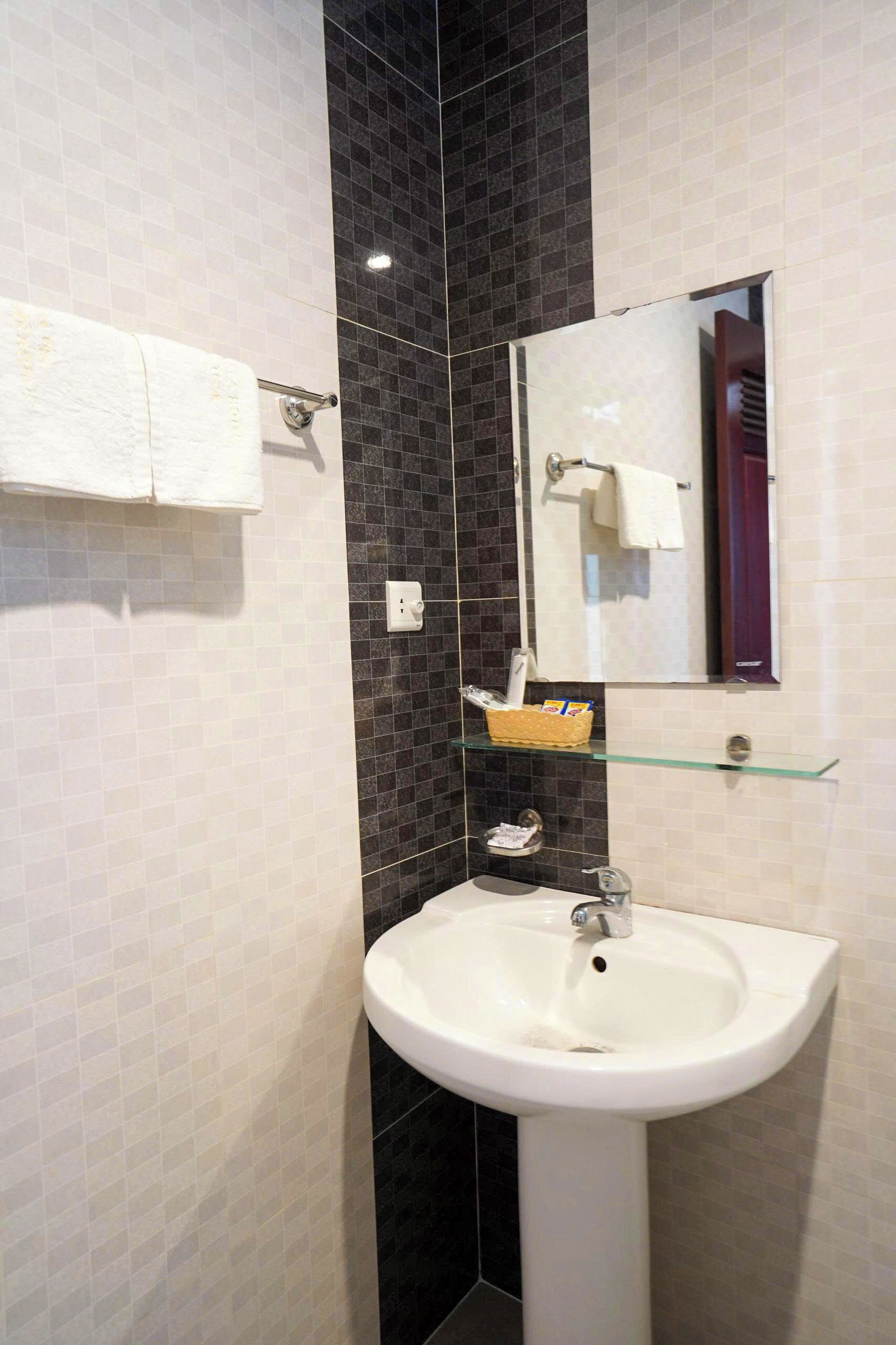A bathroom with a white sink, dark tiled walls, a mirror, and a towel rack.