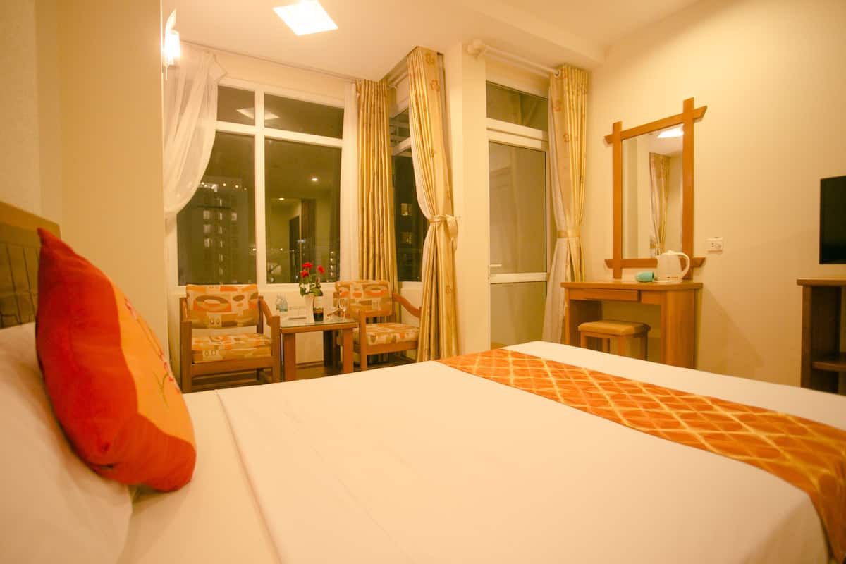 Een hotelkamer met een bed, een bureau, een stoel, een spiegel en een raam met gordijnen.
