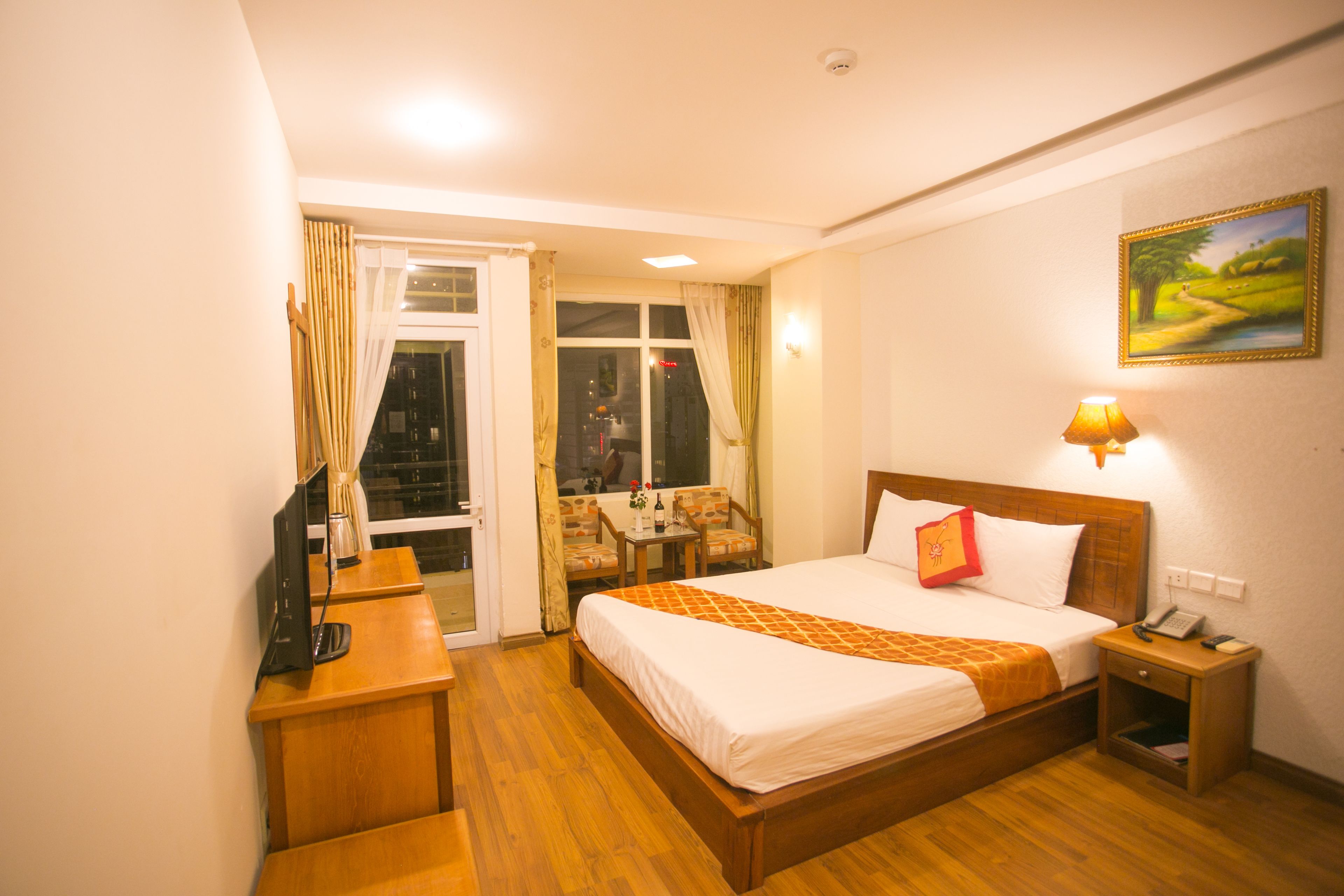 Une chambre d’hôtel avec un lit en bois, un bureau avec un ordinateur, une petite table avec des chaises et une fenêtre avec des rideaux.
