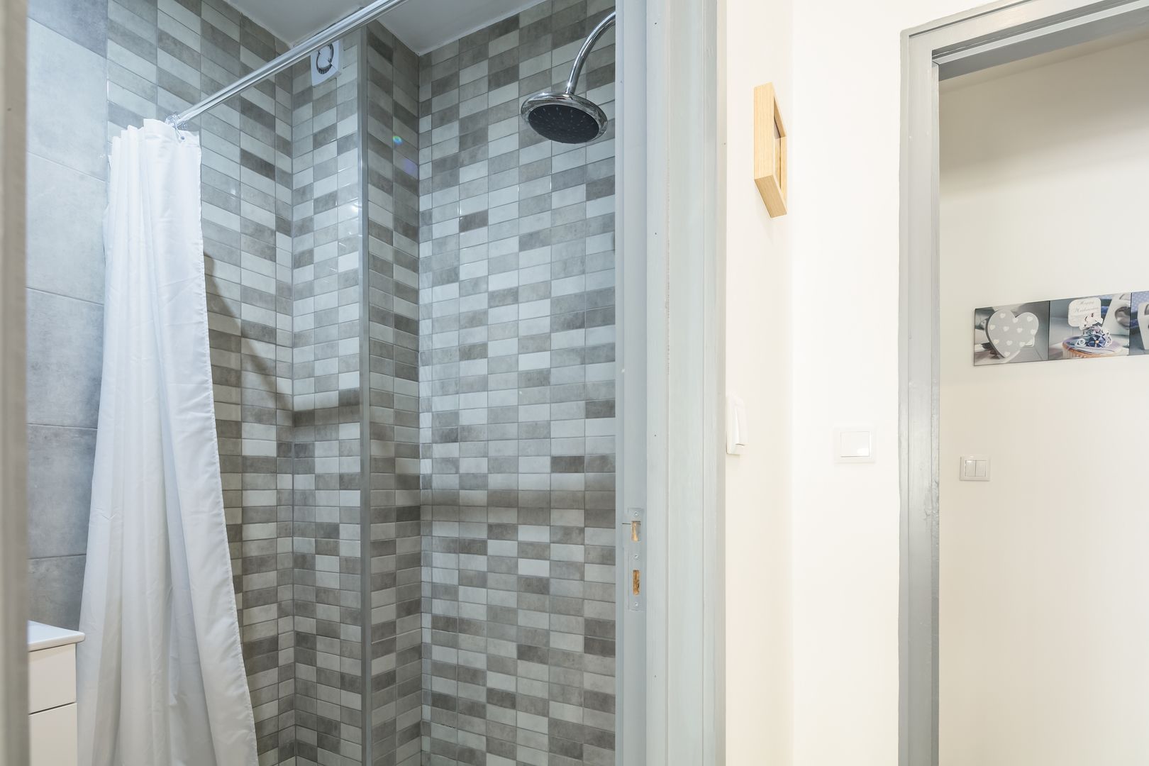 A shower with a white curtain, tiled walls, and a showerhead.