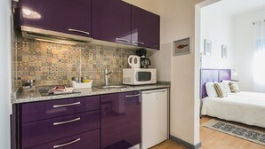 Una cocina compacta con armarios morados, un salpicadero con diseño, un microondas blanco y un lavavajillas pequeño.