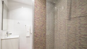 Un baño con lavamanos blanco, un espejo y una ducha con pared de azulejos estampados.