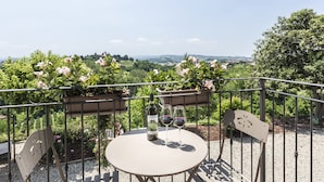 Une table ronde avec une bouteille de vin et deux verres, placée sur un balcon donnant sur un vignoble.