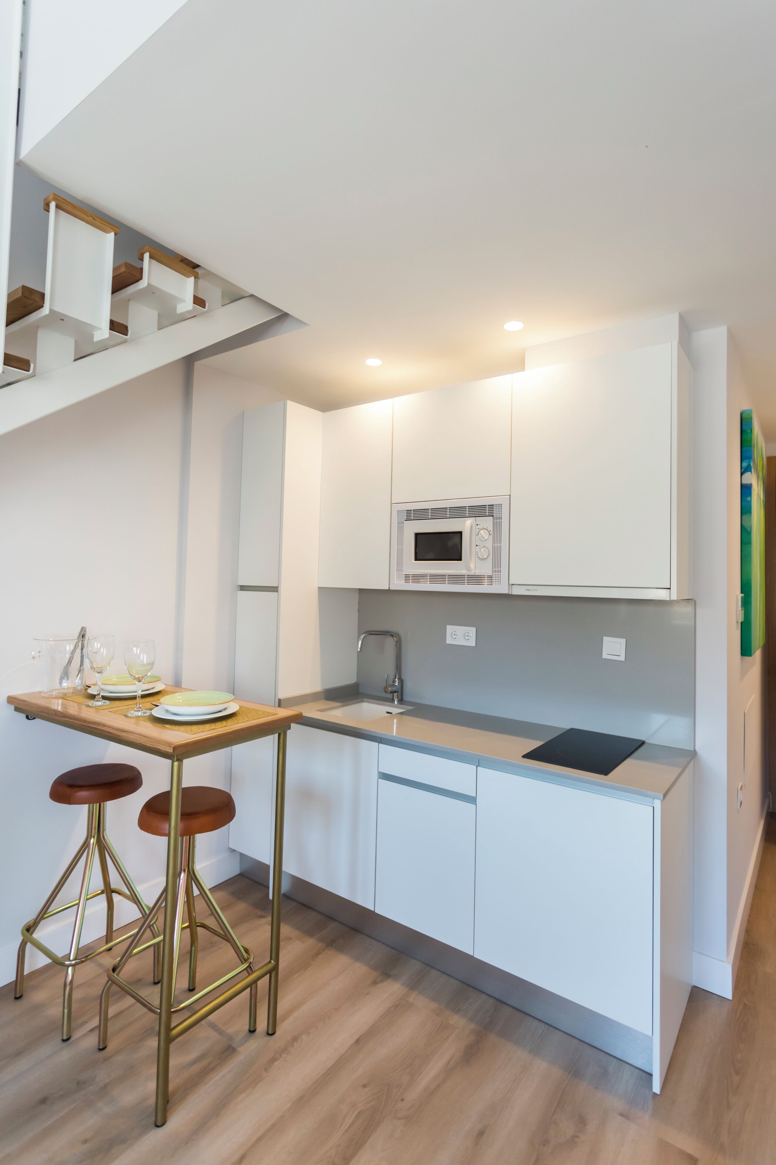 Una cocina moderna con armarios blancos, encimera de madera, microondas integrado y una mesa de comedor de madera con taburetes.