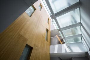 Un edificio moderno con fachada de madera, ventanas grandes y balcón de vidrio.