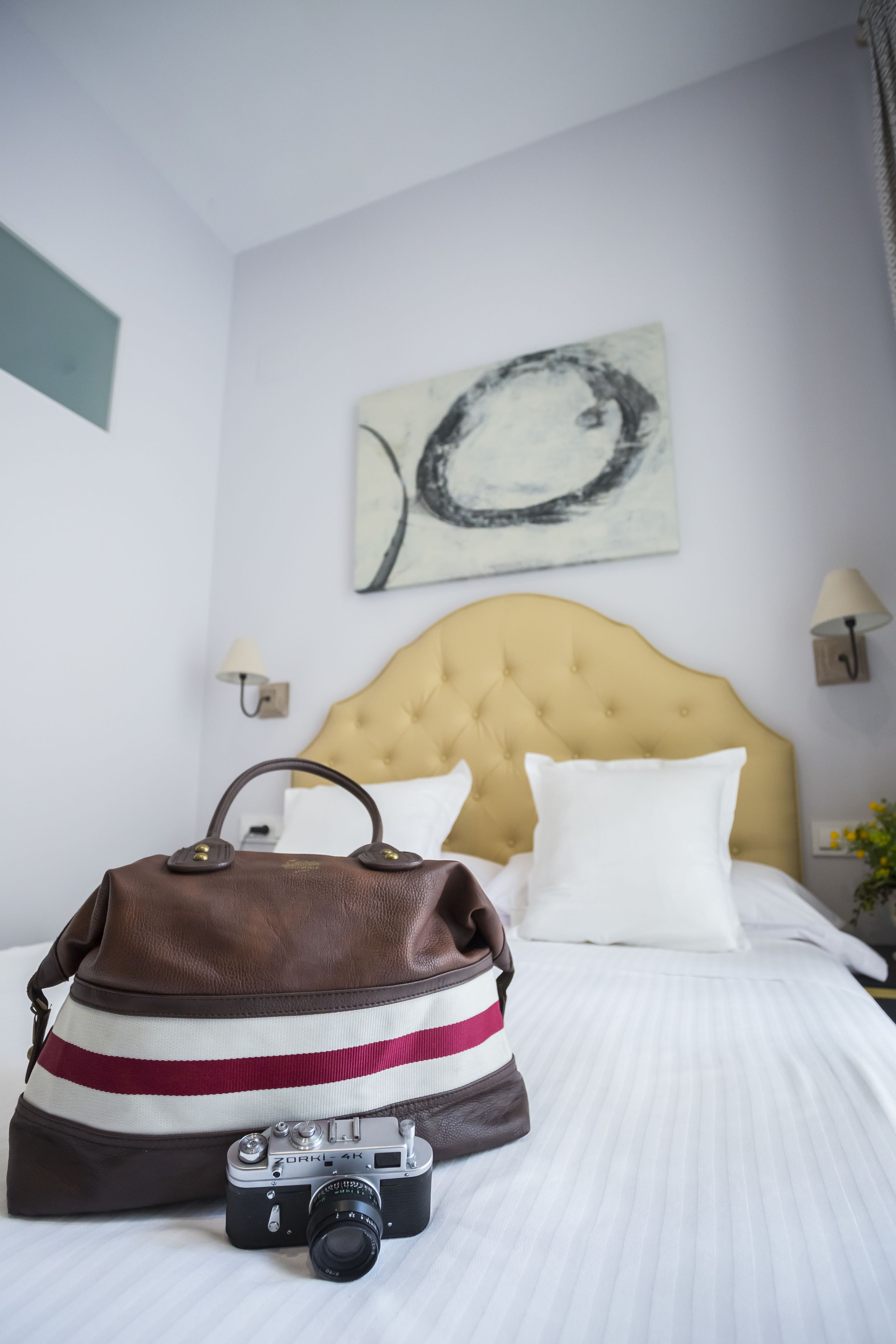 A neatly made bed with a headboard, a camera, and a handbag on the bed.